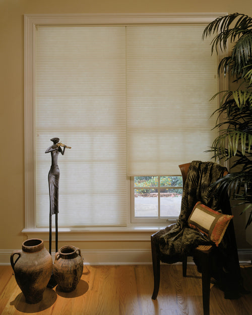 Light filtering cellular shades in a cream tone on a tall living room window beside a smaller window